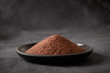 Indian Black salt Kala namak in bowl on black background. Close up. Useful for vegetarians as a source of iron. Ideal for Indian cuisine.