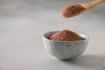 Pouring Indian Black salt Kala namak in bowl on gray background. Close up. Useful for vegetarians...