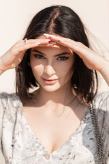 Beautiful young woman with a bob haircut in a fashionable vintage dress covers her blue eyes on a sunny day and looks at the camera