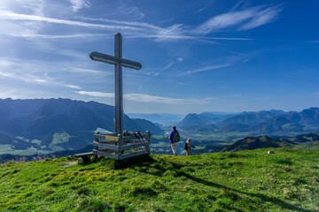 Wandern in Tirol Nähe Walchsee: Die Berge vom Zahmen und der Wilden Kaiser - Blick vom Gipfelkreuz Brennköpfl Richtung Inntal mit zwei Wanderern - obrazy, fototapety, plakaty