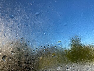 a steamed up window with dewdrops in front of nature background and blue sky