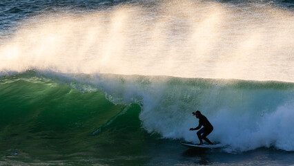 Silhouette of a surfer riding a wave with lots of spray