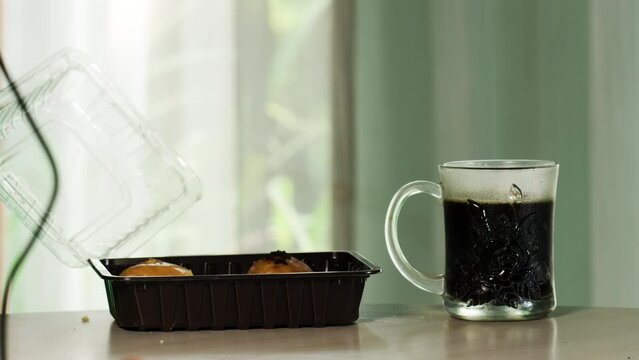 A box of banana balls with chocolate topping side by side with a glass of hot coffee