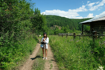 Girl tourist stands on a summer day on a rural road in full growth.