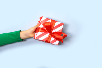 Caucasian kid child hand holds gift box on light background. Copy space for design or text. Banner. Christmas New Year mockup template.
