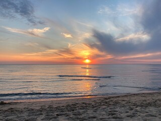 at the sea the red-golden sun shines out from behind the clouds before it sets