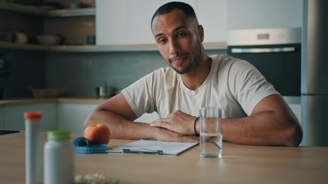 African American man guy male sports athlete nutritionist specialist sitting at table in kitchen writing prescription sport fitness diet on paper count calories looking at camera talking answer talk