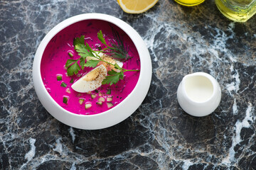 Cold beetroot soup with kefir served in a white bowl, high angle view on a black marble background,...