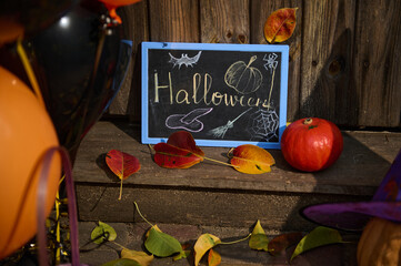 Close-up of a chalkboard with lettering Halloween, a pumpkin on the wooden doorstep with dry autumn...