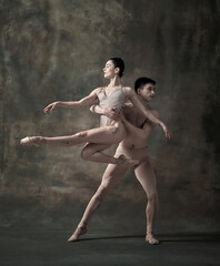 Young man and woman, ballet dancers performing isolated over dark green vintage background. Graceful artists