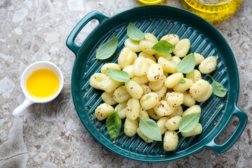 Green serving tray with potato gnocchi, fresh basil leaves and olive oil on a light-brown granite background, high angle view