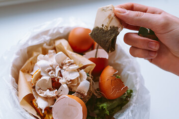 Women's hands throw tea bag into trash can.