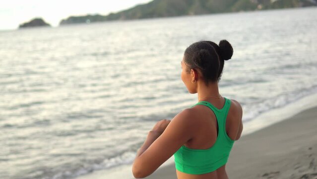 Young woman, with Afro hair, in sportswear stretching after workout at the beach