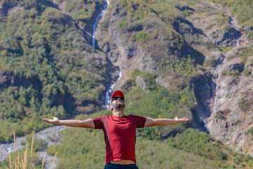 A male tourist rejoices in a trip to the mountains, spreading his arms wide.