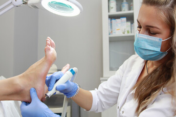 A pedicure master treats the heel with a power tool in a beauty salon.