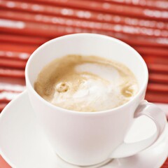 Cup of frothy cappuccino coffee on a saucer on a red bamboo table