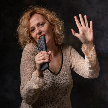 A blonde woman simulates singing at a concert using a remote control as a microphone