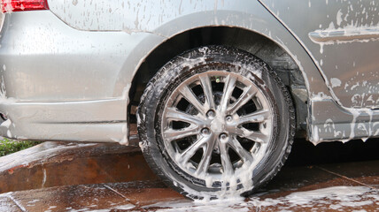 Black car tire is being washed and covered by washing foam in a car care shop                              