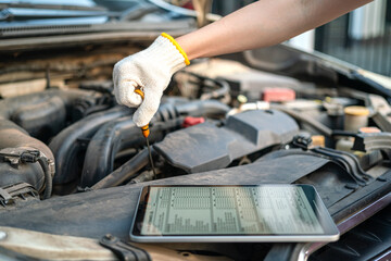 A repairman is checking car engine lube oil level, using the checklist document in the digital tablet device. Industrial and transportaion occupation working scene, selective focus.