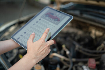 Using the vehicle checklist guideline on the digital tablet during perform preventive maintenance with car engine part as blurred background. Transportation service and maintenance working action.