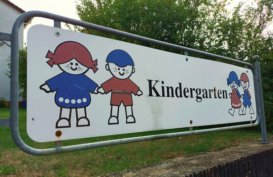 Weißes Schild Kindergarten mit stilisierten Kindern mit roten und blauen Kleidern. 