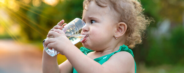 The child drinks water from a glass. Selective focus.