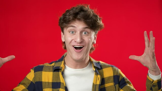 Handsome thinking young man 20s, looks at camera gives mind blown gesture showing explosion of ideas posing on red background.