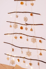 A creative Christmas tree made of branches decorated with dry orange slices and wooden  figurines on the wall in the home interior.Eco-friendly New Year and Christmas decor.