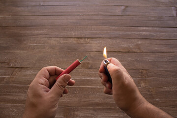 Image of the hands of a man who lights the fuse of a firecracker with a lighter. Reference you have...