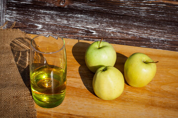 A glass of freshly squeezed apple juice and a green ripe apples on a table covered with a cloth...
