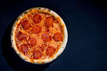 Pizza with tomato sauce, mozzarella, salami on black background. View from above, copy space