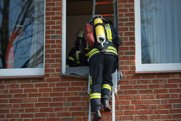 Firefighter with breathing apparatus climbs up a ladder to the window of a house