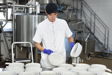A worker in medical gloves shows the process of producing cottage cheese at a dairy factory.