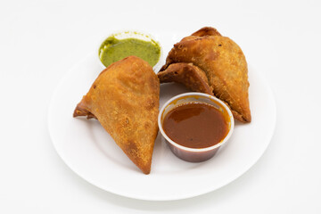 Two Vegetable Samosas with Mint and Tamarind Chutneys on a White Plate
