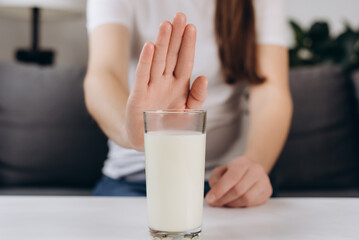 Lactose intolerance concept. Close up of young woman pushing glass of milk deny to drink. Unhealthy...