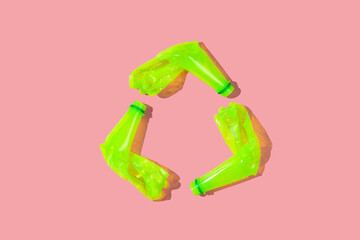 Recycle symbol made of used acid colored plastic bottles isolated on pink background. Flat lay...