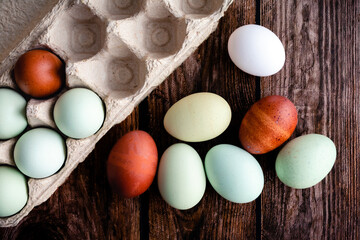 Blue, Green, and Brown Heritage Eggs With an Egg Carton On a Rustic Wood Background: Overhead view of a group of multicolored eggs on a wooden table