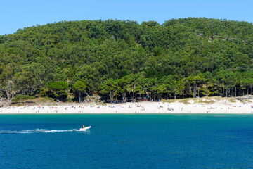 view from the sea to the beach and people on the sand on a clear sunny day