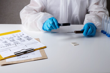 Forensic scientist doing fingerprint analysis in police crime lab, examining a knife with a...