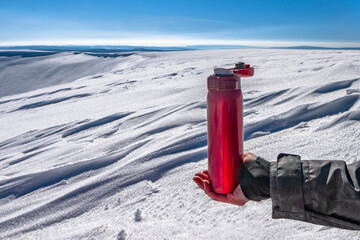 Red thermo bottle for winter leisure. Flask thermos of drinks on hand on background of winter mountains landscape