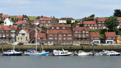 LANDSCAPE OF WHITBY TOWN NEAR THE RIVER  , RED BROWN HOUSES ,ROOF TILE AND WHITE FRAME WINDOWS AND  FISHING BOATS AT DOCK.UK URBAM PLANNING