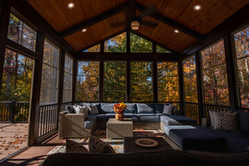Cozy screened porch enclosure with contemporary furniture at Thanksgiving Holiday. Porch door open, flower bouquet in a vase, autumn leaves and woods in the background.