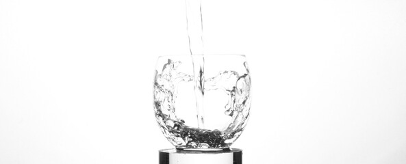 A close up shot of clean, fresh water being poured into a clear glass, and splashing up the sides of the glass. Image has concept of health and wellness, and has copy space.