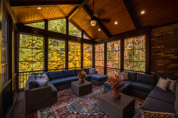 Cozy screened porch enclosure with contemporary furniture at Thanksgiving Holiday. Flower bouquet in a vase, autumn leaves and woods in the background.