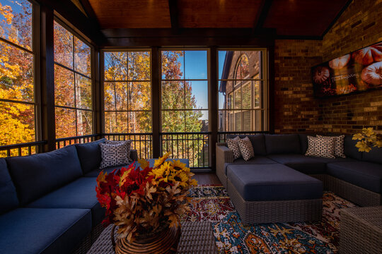 Cozy screened porch enclosure with contemporary furniture at Thanksgiving Holiday. Flower bouquet in a vase, autumn leaves and woods in the background.