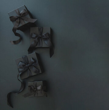 Black Friday sales concept. Four gift box, black satin ribbon on black background, top view.