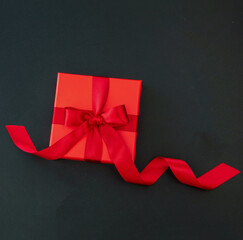 Black Friday Birthday Valentines day. Red gift box red ribbon on black background, top view, space.