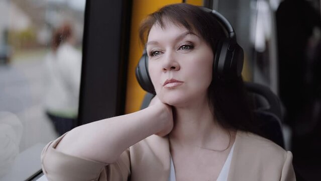 Woman in headphones rides in public transport, looks out the window and listens to music