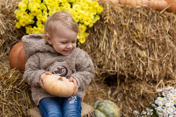 A small child holds a pumpkin in his hands on a background of hay