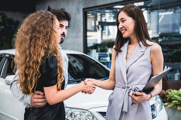 Couple is picking up a car from a garage employee delivers the car to the customer and shakes hands...